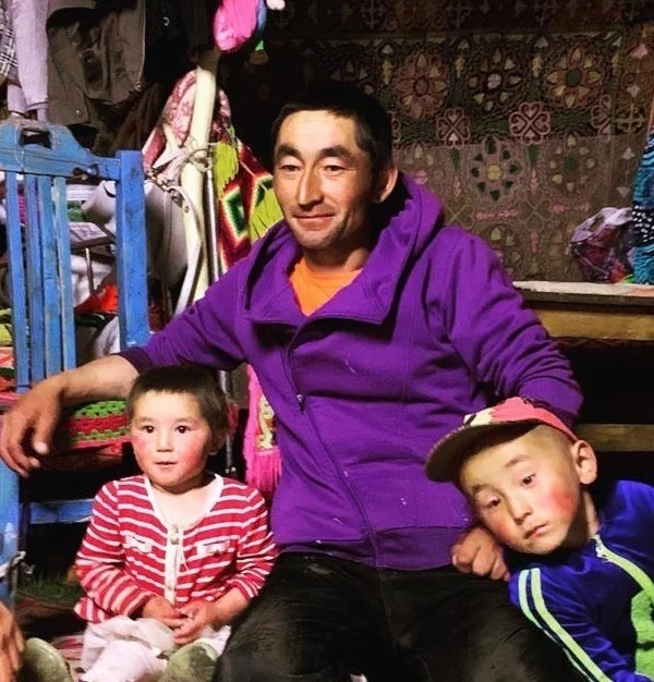 A horse guide in a purple hoodie sitting inside a decorated ger with two young children