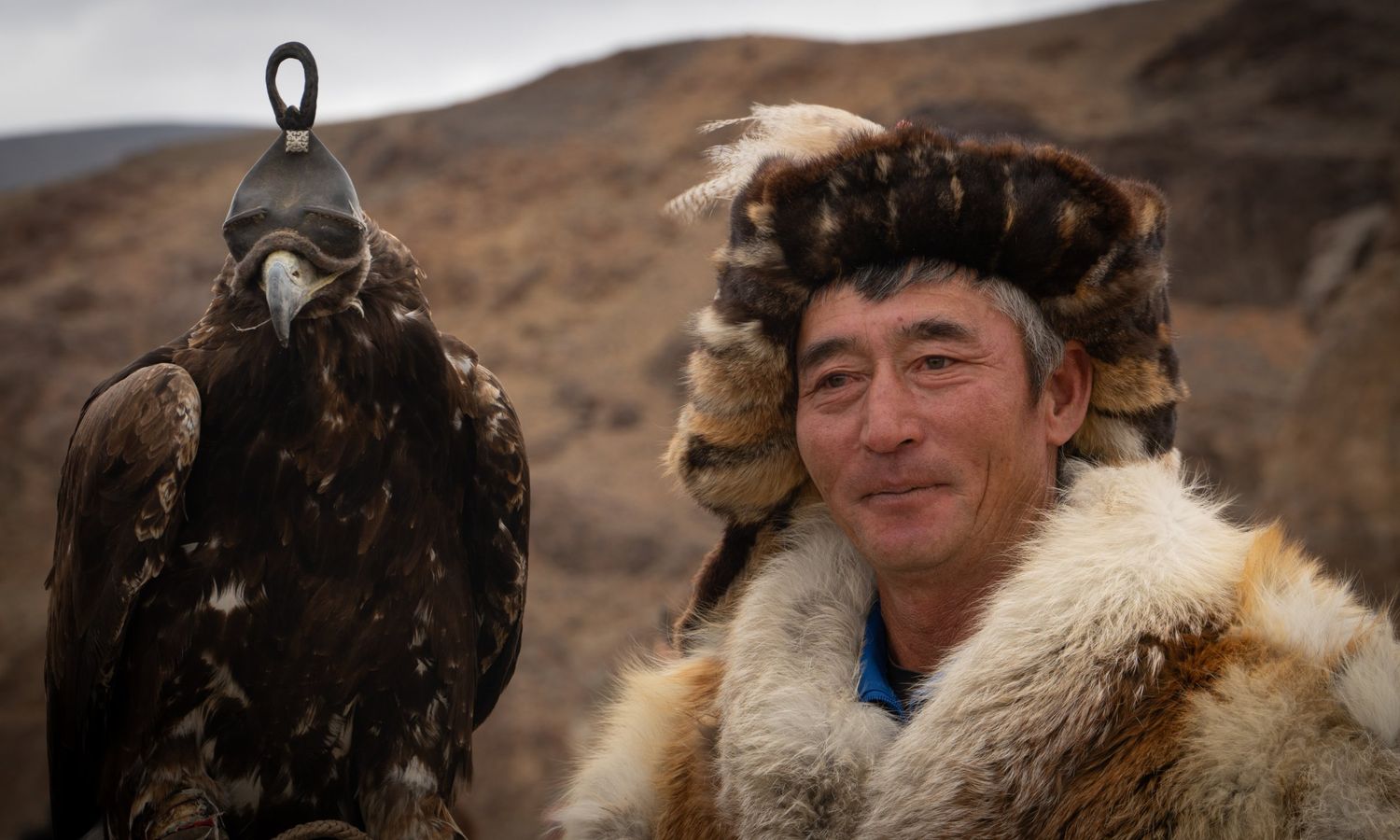 Kazakh eagle hunter with a hooded golden eagle at the Golden Eagle Festival