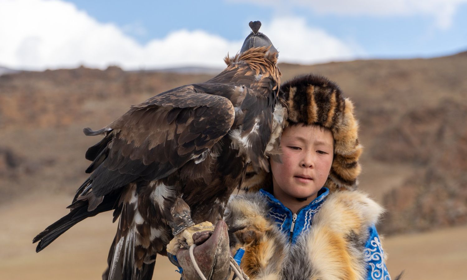 Young Kazakh eagle hunter in traditional dress holding a golden eagle