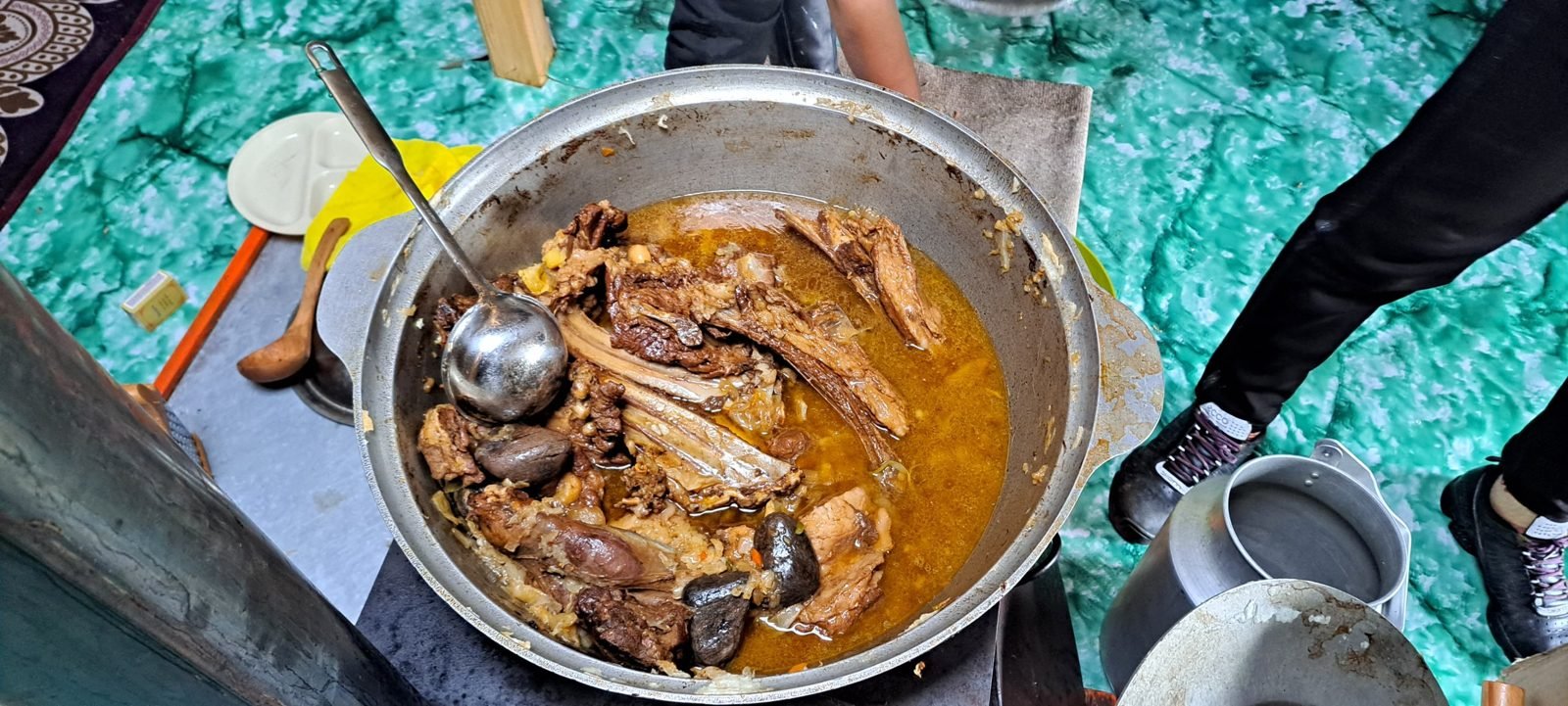 A large pot of slow-cooked meat and ribs in broth with a ladle, on a ger stove