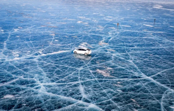A car and two people on the cracked blue ice of frozen Tolbo Lake